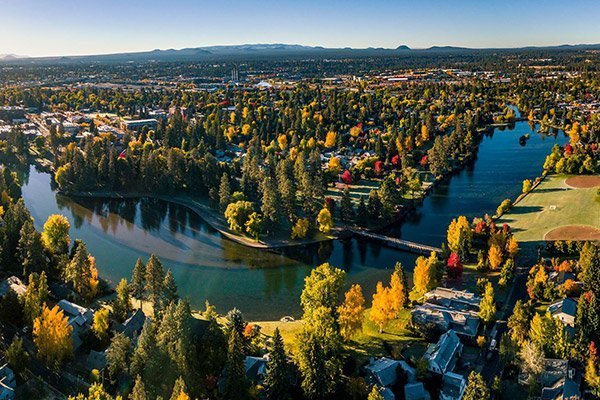 An aerial view of Bend, Oregon in autumn with fall foliage and the Deschutes River winding through it.