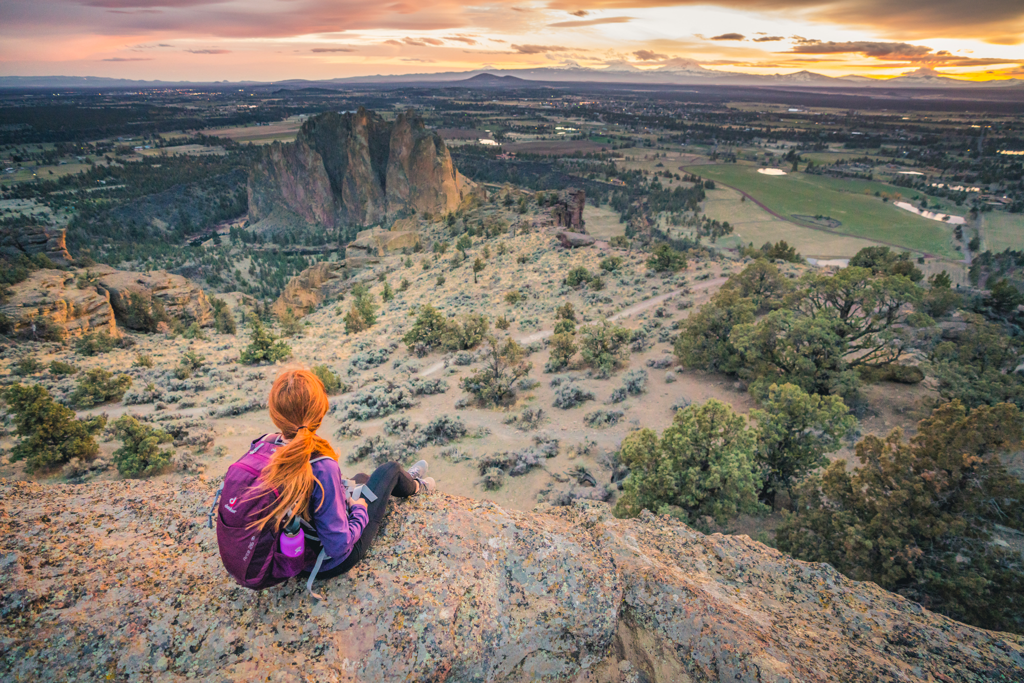 A female hiker sitting at the top of Pilot Butte in Bend and looking out over the landscape of Bend, Oregon