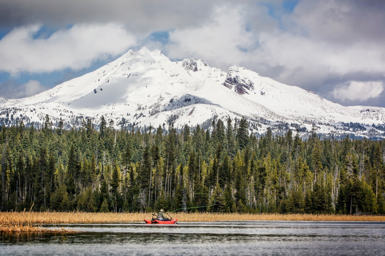 A boat and fisherman fishing on Cascade Lakes in Bend, Oregon with a snowy Mt. Bachelor in the background.