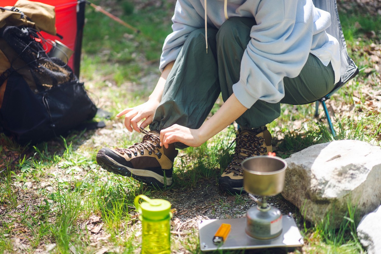Close up of a woman hiker bending down to tie her hiking boot with hiking gear and backpack in the background. 